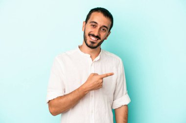 Mavi arka planda izole edilmiş genç beyaz adam gülümsüyor ve boş alanda bir şeyler gösteriyor..