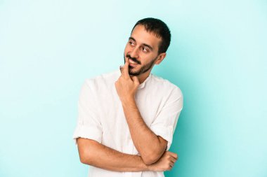 Mavi arka planda izole edilmiş genç beyaz adam rahatlamış bir şeyin fotokopi odasına baktığını düşünüyor..