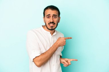 Mavi arka planda izole edilmiş genç beyaz adam işaret parmağıyla fotokopi alanını işaret ederek şok oldu..