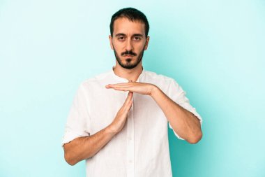 Mavi arka planda izole edilmiş genç beyaz bir adam bir mola hareketi gösteriyor..