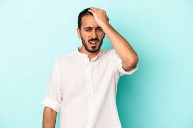 Kafkasyalı genç adam mavi arka planda izole edilmiş bir şekilde bir şeyi unutuyor. Alnına avuç içi ve gözlerini kapayarak vuruyor..