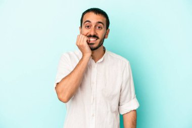 Mavi arka planda izole edilmiş, tırnak yiyen, gergin ve endişeli genç bir beyaz adam..