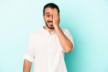 Mavi arka planda izole edilmiş genç beyaz adam yüzünün yarısını palmiye ile kaplayarak eğleniyor..