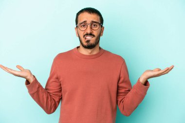 Kafkasyalı genç adam mavi arka planda izole edilmiş. Kafası karışmış ve omuz silkiyor. Kopya alanını tutmak için..