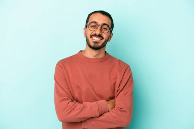 Mavi arka planda kendini güvende hisseden, kararlılıkla kollarını kavuşturan genç beyaz bir adam..