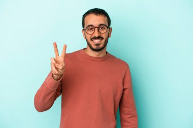 Kafkasyalı genç adam mavi arka planda izole edilmiş neşeli ve kaygısız parmaklarıyla barış sembolü gösteriyor..