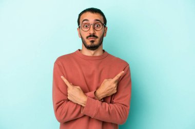 Mavi arka plan noktalarında izole genç beyaz adam, iki seçenek arasında seçim yapmaya çalışıyor.