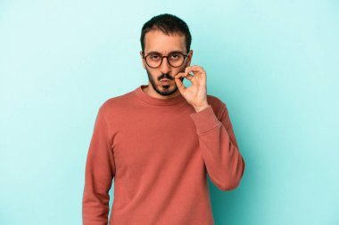 Genç beyaz adam mavi arka planda izole edilmiş ve parmakları dudaklarında bir sır saklıyor..