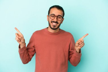 Mavi arka planda izole edilmiş genç beyaz adam farklı kopya alanlarını gösteriyor, birini seçiyor, parmaklarıyla gösteriyor.