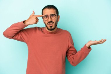 Kafkasyalı genç adam mavi arka planda izole edilmiş ve elinde bir ürün tutuyor..