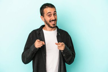 Mavi arka planda izole edilmiş genç beyaz adam parmaklarıyla ön tarafı işaret ediyor..