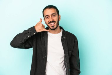 Mavi arka planda izole edilmiş genç beyaz adam parmaklarıyla bir cep telefonu hareketi gösteriyor..