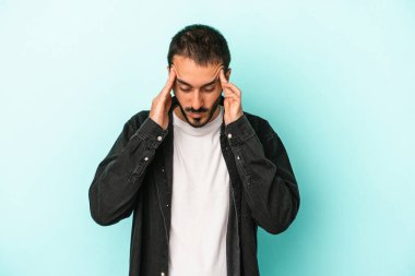 Genç beyaz adam mavi arka planda izole edilmiş tapınaklara dokunuyor ve başı ağrıyor..