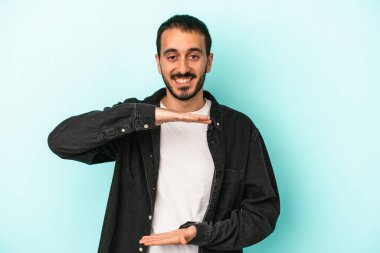 Mavi arka planda izole genç beyaz adam iki eliyle bir şey tutuyor, ürün sunumu..