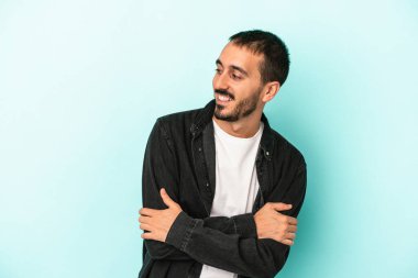 Mavi arka planda izole edilmiş genç beyaz adam kollarını kavuşturarak gülümsüyor..