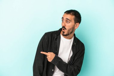 Kafkasyalı genç adam mavi arka plan noktalarında izole edilmiş başparmak uzakta, gülüyor ve kaygısız.