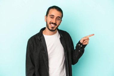 Mavi arka planda izole edilmiş genç beyaz adam işaret parmağıyla işaret ederek gülümsüyor..