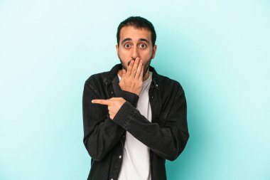 Mavi arka planda izole edilmiş genç beyaz adam yan tarafı işaret ediyor.