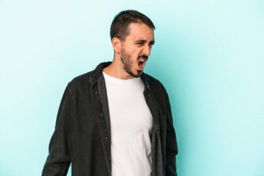 Kafkasyalı genç adam mavi arka planda izole edilmiş. Çok kızgın, öfkeli, hayal kırıklığına uğramış..