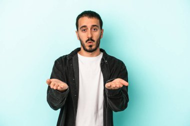 Kafkasyalı genç adam mavi arka planda izole edilmiş dudaklar kıvrılıyor ve hava öpücüğü göndermek için avuç içleri tutuyor..