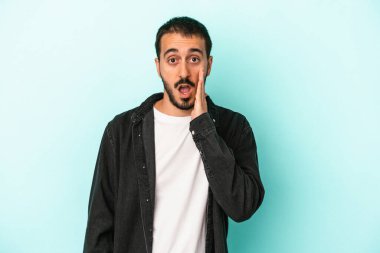 Mavi arka planda izole edilmiş genç beyaz adam yüksek sesle bağırıyor, gözleri açık ve elleri gergin tutuyor..