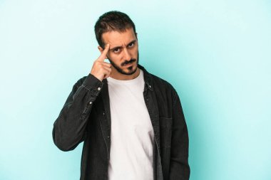 Mavi arka planda izole edilmiş genç beyaz bir adam şakağı parmağıyla işaret ediyor, düşünüyor ve bir göreve odaklanıyor..