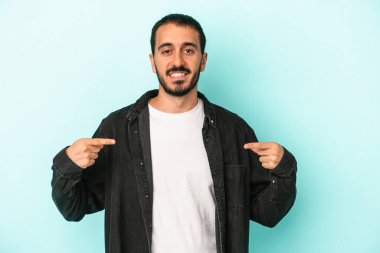 Kafkasyalı genç adam mavi arka planda izole edildi. Parmakları aşağıda, olumlu bir his var..