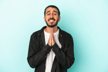 Mavi arka planda izole edilmiş genç beyaz bir adam el ele tutuşup, ağzının kenarında dua ediyor, kendinden emin..