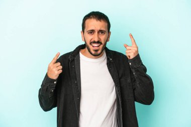 Mavi arka planda izole edilmiş genç beyaz adam işaret parmağıyla bir hayal kırıklığı jesti gösteriyor..