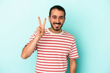 Mavi arka planda izole edilmiş genç beyaz adam iki numarayı parmaklarıyla gösteriyor..