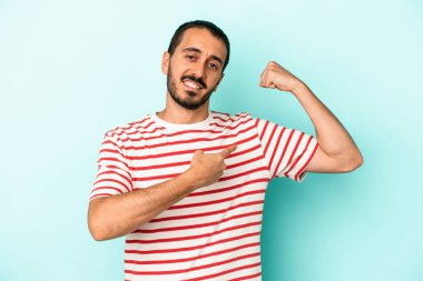 Mavi arka planda izole edilmiş genç beyaz adam güçlü bir hareket sergiliyor kollarıyla, kadınsı gücün sembolü.