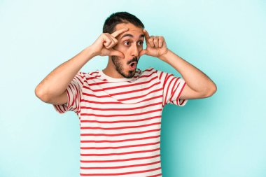 Mavi arka planda izole edilmiş genç beyaz adam bir başarı fırsatı bulmak için gözlerini açık tutuyor..