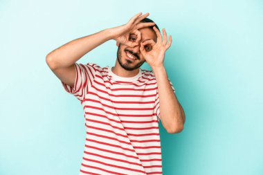 Mavi arka planda izole edilmiş genç beyaz adam gözlerinde sorun olmadığını gösteriyor.