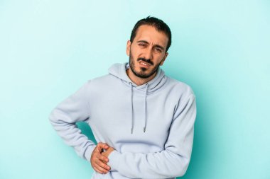 Mavi arka planda karaciğer ağrısı çeken, karnı ağrıyan genç beyaz bir adam..
