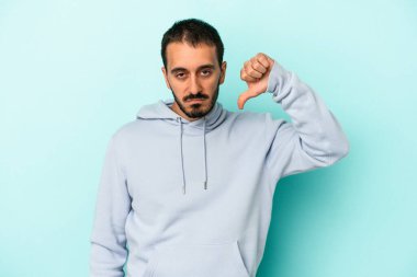 Mavi arka planda izole genç beyaz adam baş parmağını aşağı gösteriyor, hayal kırıklığı konsepti.