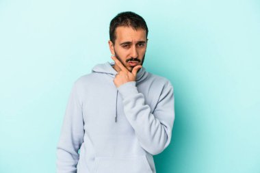 Kafkasyalı genç bir adam mavi arka planda izole edilmiş. Bir strateji planlıyor, bir iş yolu düşünüyor..