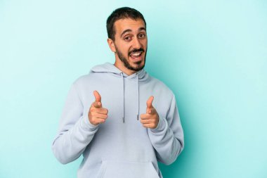 Mavi arka planda izole edilmiş genç beyaz adam parmaklarıyla ön tarafı işaret ediyor..