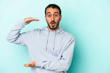 Mavi arka planda izole genç beyaz adam iki eliyle bir şey tutuyor, ürün sunumu..