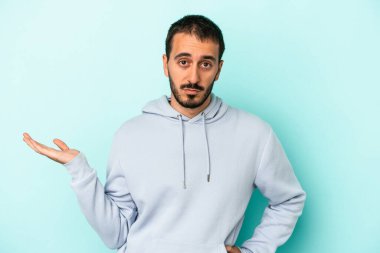 Mavi arka planda izole edilmiş genç beyaz bir adam bir palmiye üzerinde fotokopi alanı ve belinde bir el daha gösteriyor..