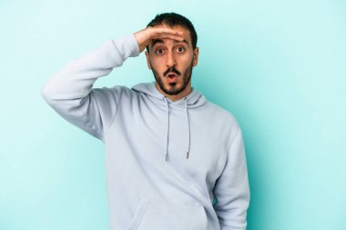 Kafkasyalı genç adam mavi arka planda izole edilmiş, uzaklara bakıyor ve elini alnına koyuyor..