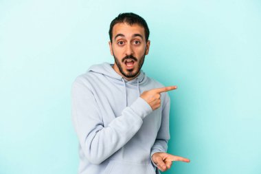 Kafkasyalı genç adam mavi arka planda izole edilmiş. İşaret parmağıyla işaret ettiği için heyecanlı..