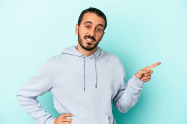 Mavi arka planda izole edilmiş genç beyaz adam işaret parmağıyla işaret ederek gülümsüyor..