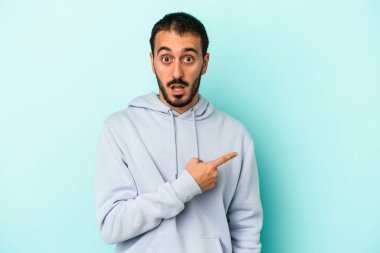 Mavi arka planda izole edilmiş genç beyaz adam yan tarafı işaret ediyor.