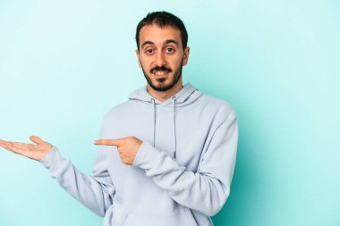 Kafkasyalı genç adam mavi arka planda izole edilmiş. Elinde palmiye ağacının bir kopyası olduğu için heyecanlı..