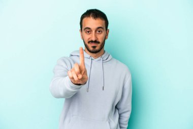 Mavi arka planda izole edilmiş genç beyaz adam bir numarayı parmağıyla gösteriyor..