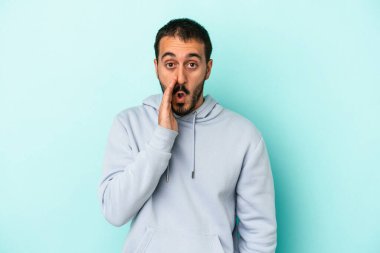 Mavi arka planda izole edilmiş genç beyaz bir adam gizli bir sıcak fren haberi veriyor ve yana bakıyor.