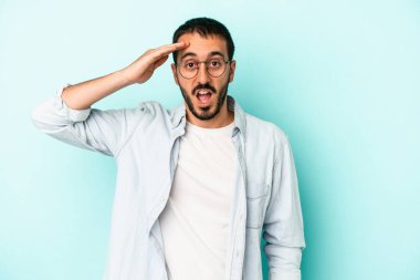 Mavi arka planda izole edilmiş genç beyaz adam yüksek sesle bağırıyor, gözleri açık ve elleri gergin tutuyor..