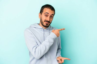 Mavi arka planda izole edilmiş genç beyaz adam işaret parmağıyla fotokopi alanını işaret ederek şok oldu..