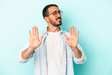 Mavi arka planda izole edilmiş genç beyaz adam elini uzatmış, dur işareti göstererek seni engelliyor..