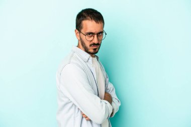 Kafkasyalı genç adam mavi arka planda izole edilmiş hoşnutsuzca kaşlarını çatmış, kollarını kavuşturmuş..